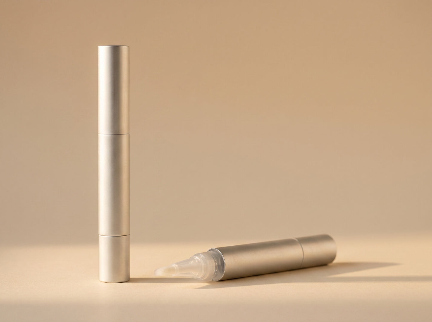 Two Botanic Cuticle Serum Travel matte-aluminum pens, one upright and one cap-off showing the fine brush tip, on a warm neutral background